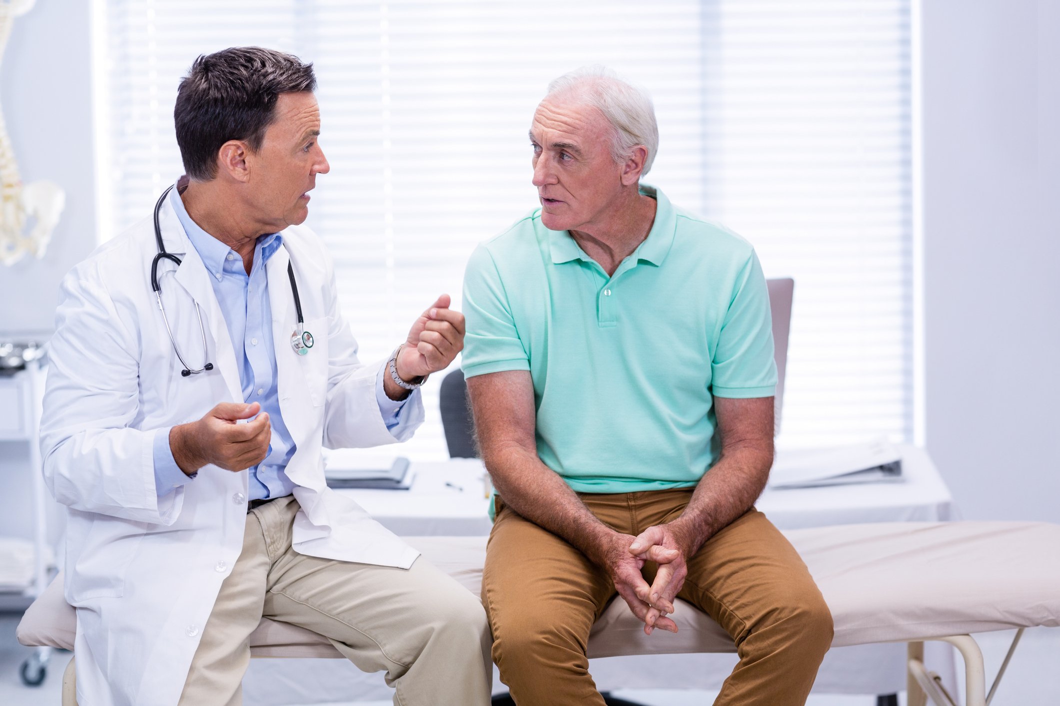 Doctor talking to senior man sitting on an exam table.