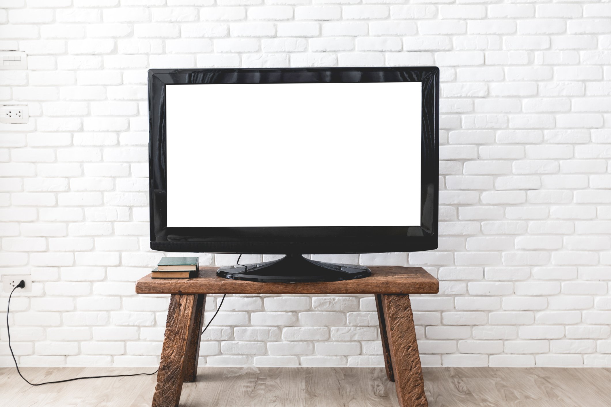 A flat screen television sitting on a wooden table against a white brick wall.