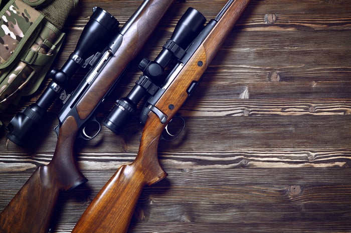 Two hunting rifles with mounted scopes lying on a wooden floor.