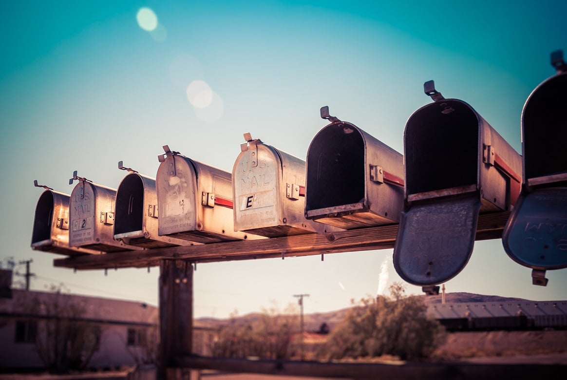 Row of mailboxes on a wood post in a rural setting.