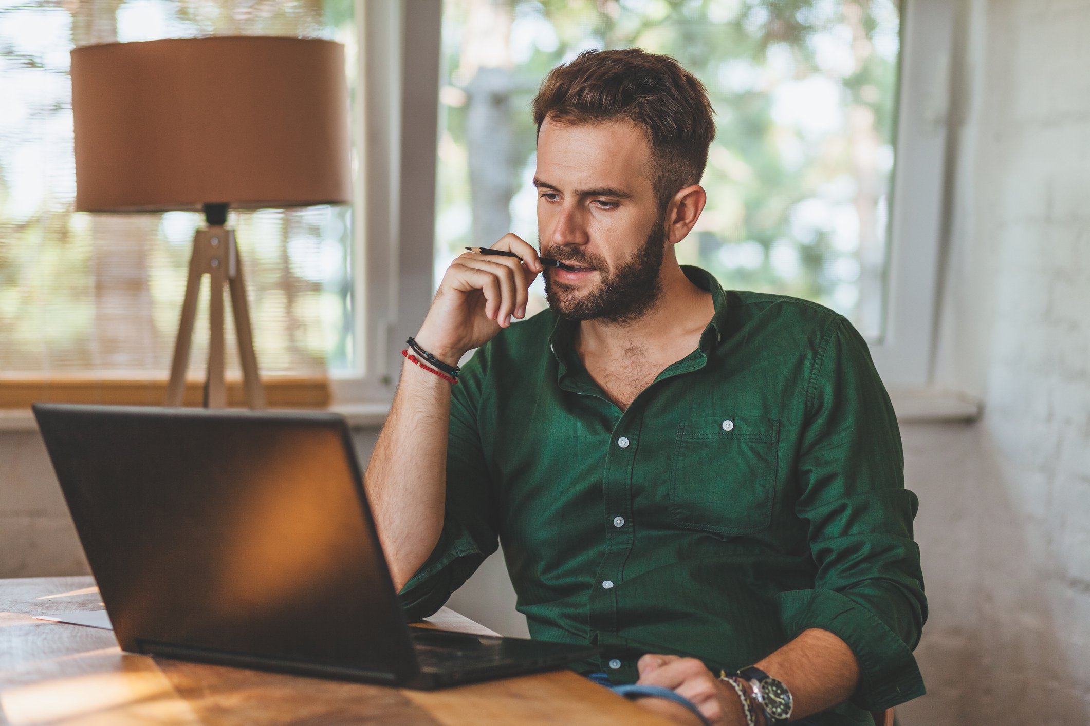 Man at laptop scratching face and staring with serious expression