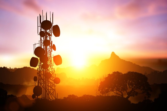 A fully stacked cell tower in silhouette against a colorful sunrise.