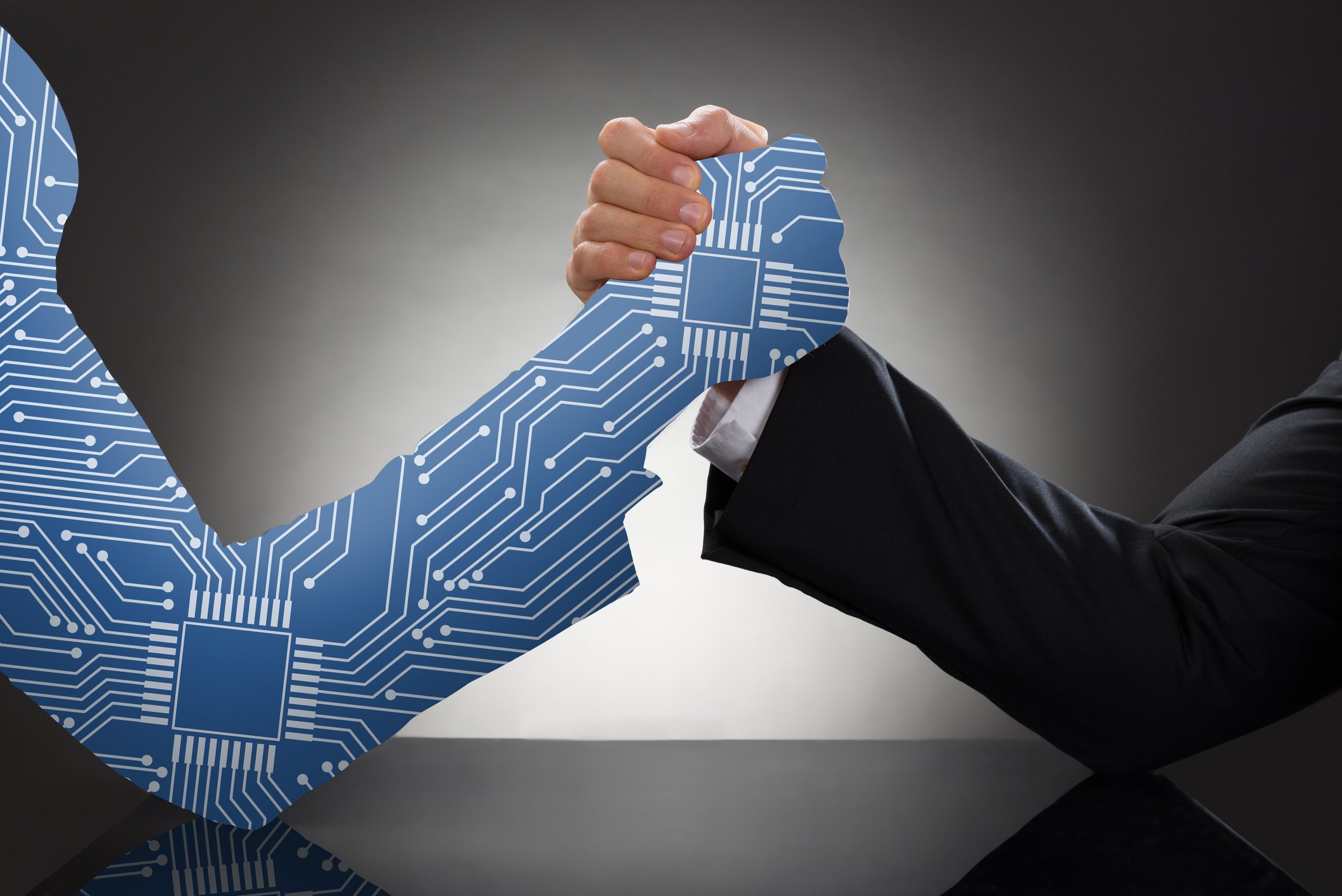 A man in a suit arm wrestles another arm made up of cartoon digital wiring. 