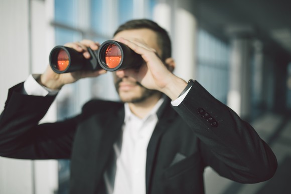 A businessman in a suit looks through binoculars.