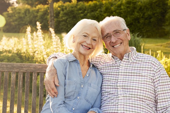 Senior couple sitting on wooden bench outdoors, smiling