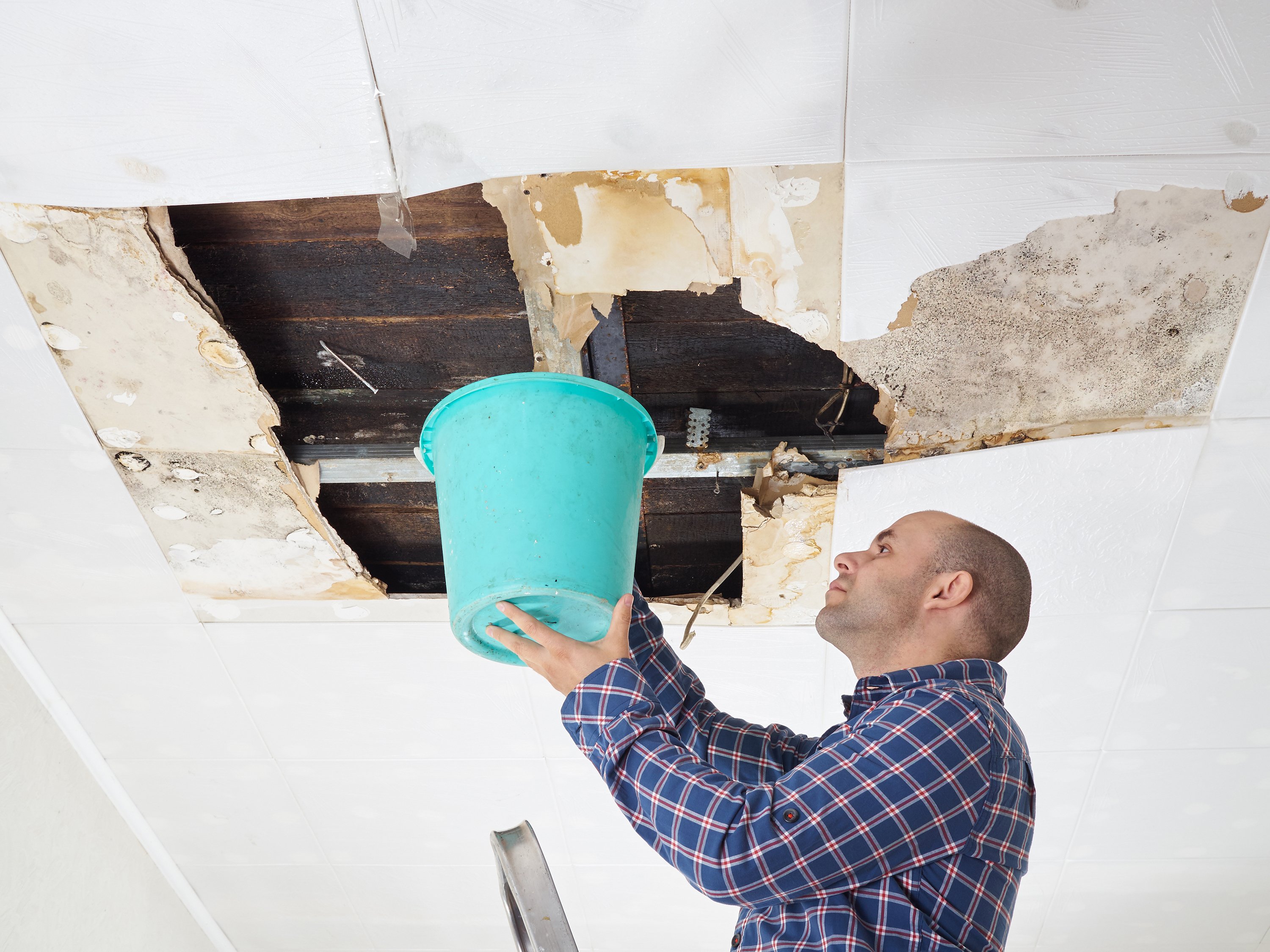 Man holding large bucket up to damaged ceiling