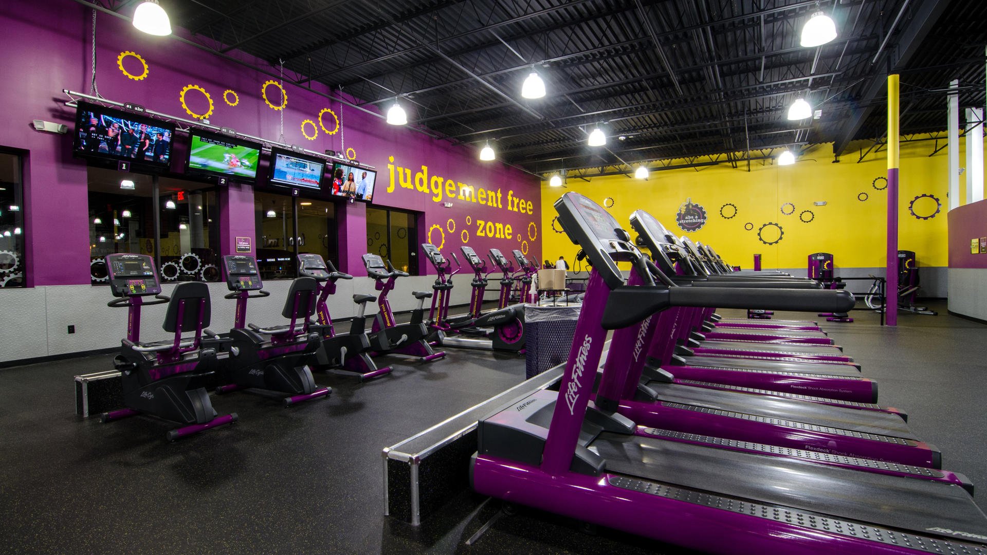 An empty gym with treadmills and other equipment near a wall that shows the Planet Fitness motto, "judgement free zone"