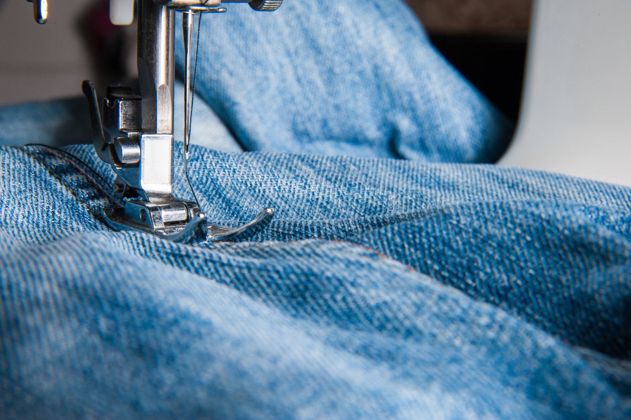 Jeans being manufactured using an industrial stitcher.