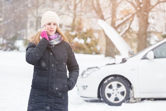 Woman in coat on phone in front of white car with its hood up