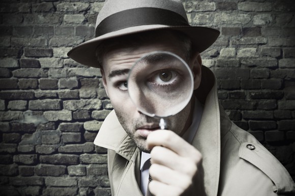 Man in detective hat looking through a magnifying glass