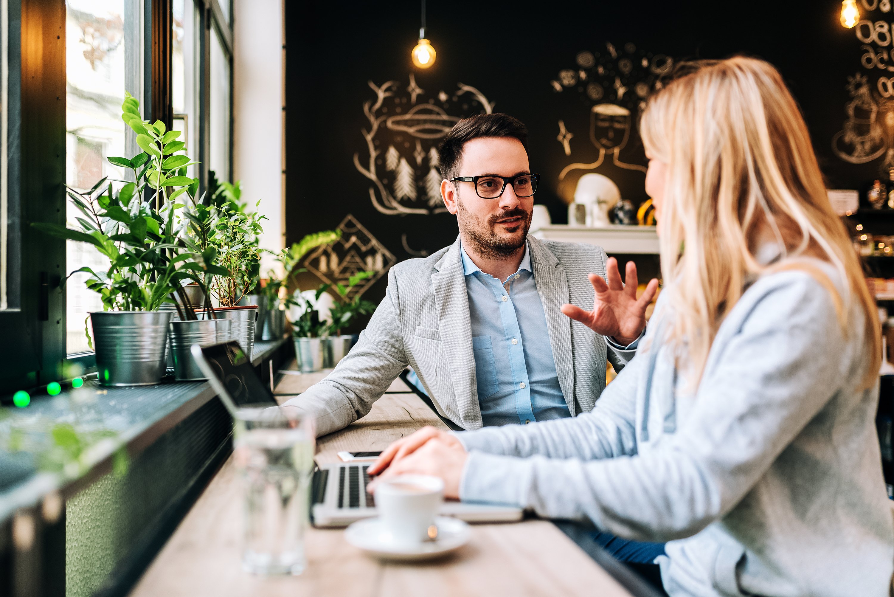 Professionally dressed woman typing on laptop while talking to professionally dressed man