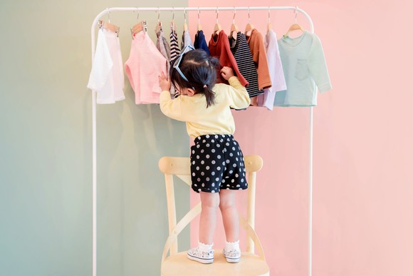 A female toddler browses through a rack of clothes.