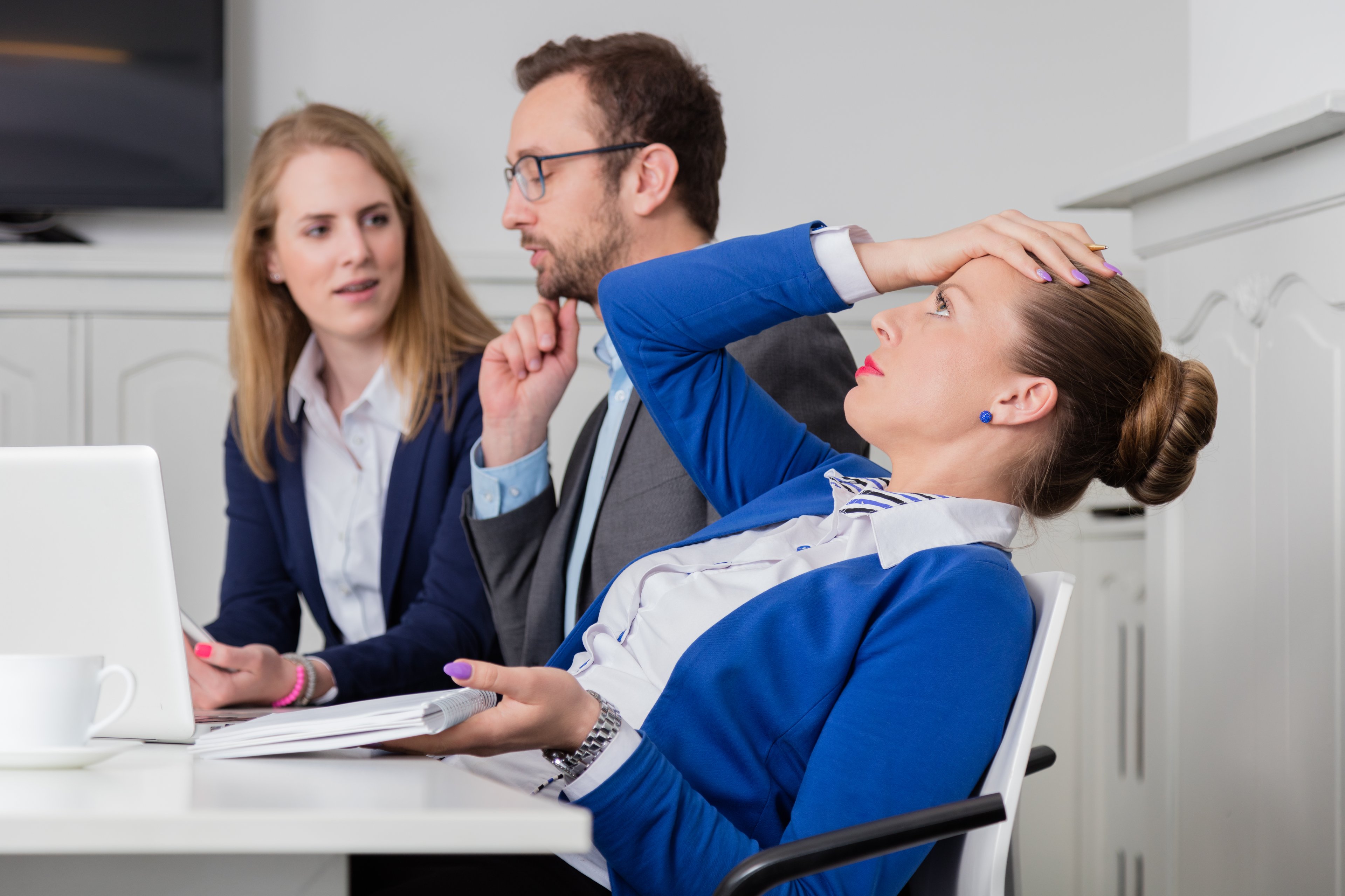 Woman leaning back in chair and holding her head with man and woman next to her