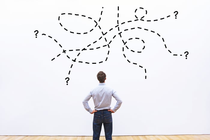 Man with hands on hips looking at a complicated drawing of lines on a wall.