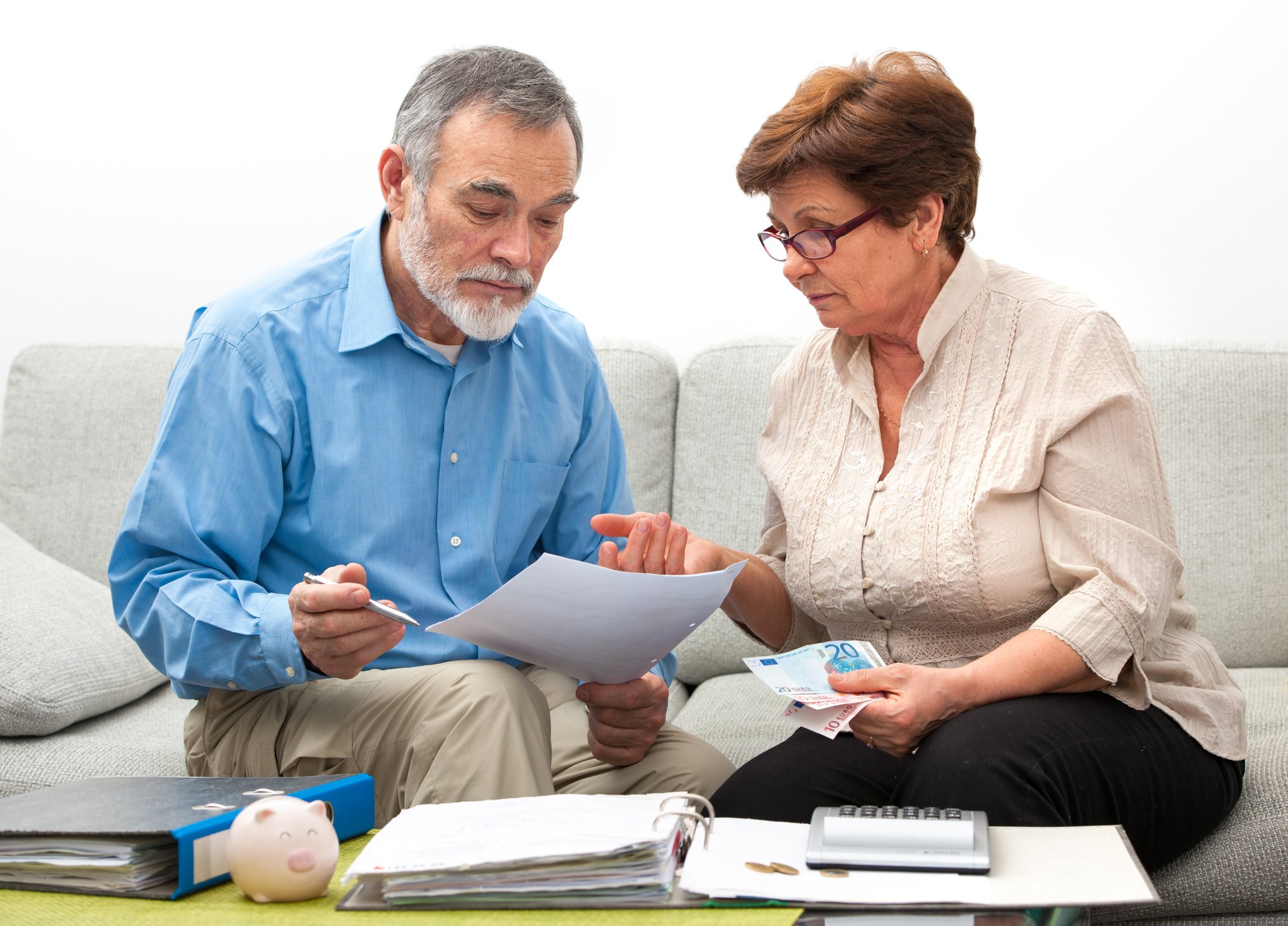 Older man and woman looking at documents; on a table in front of them are binders and a calculator