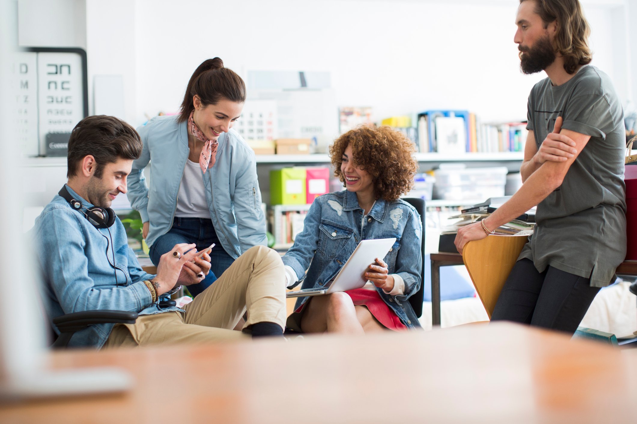 Millennial workers gathered around a conference table using smartphones and computers.