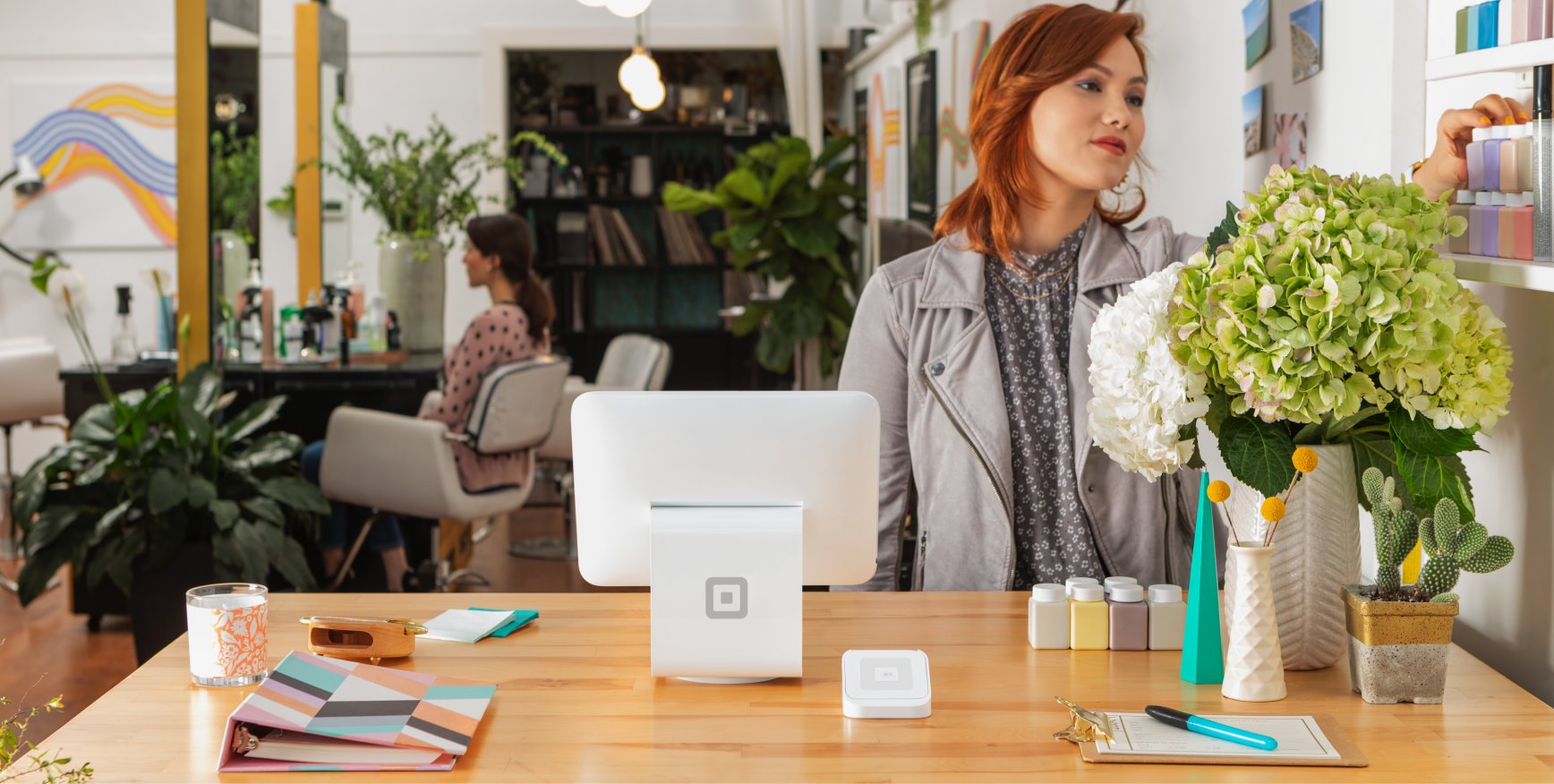 A Square register sitting on a counter with a business owner standing behind the counter.