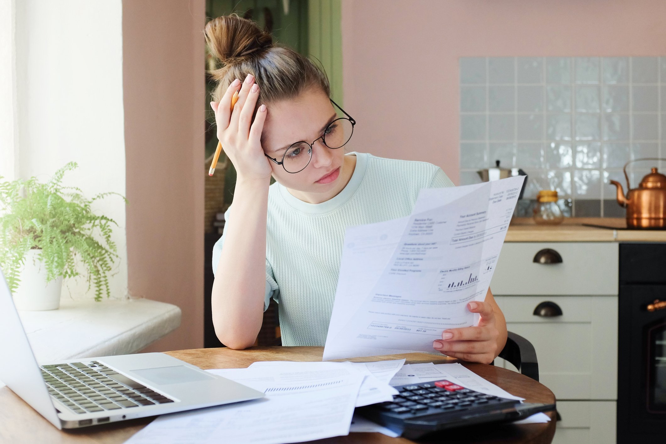 Young woman at laptop looks at documents 
