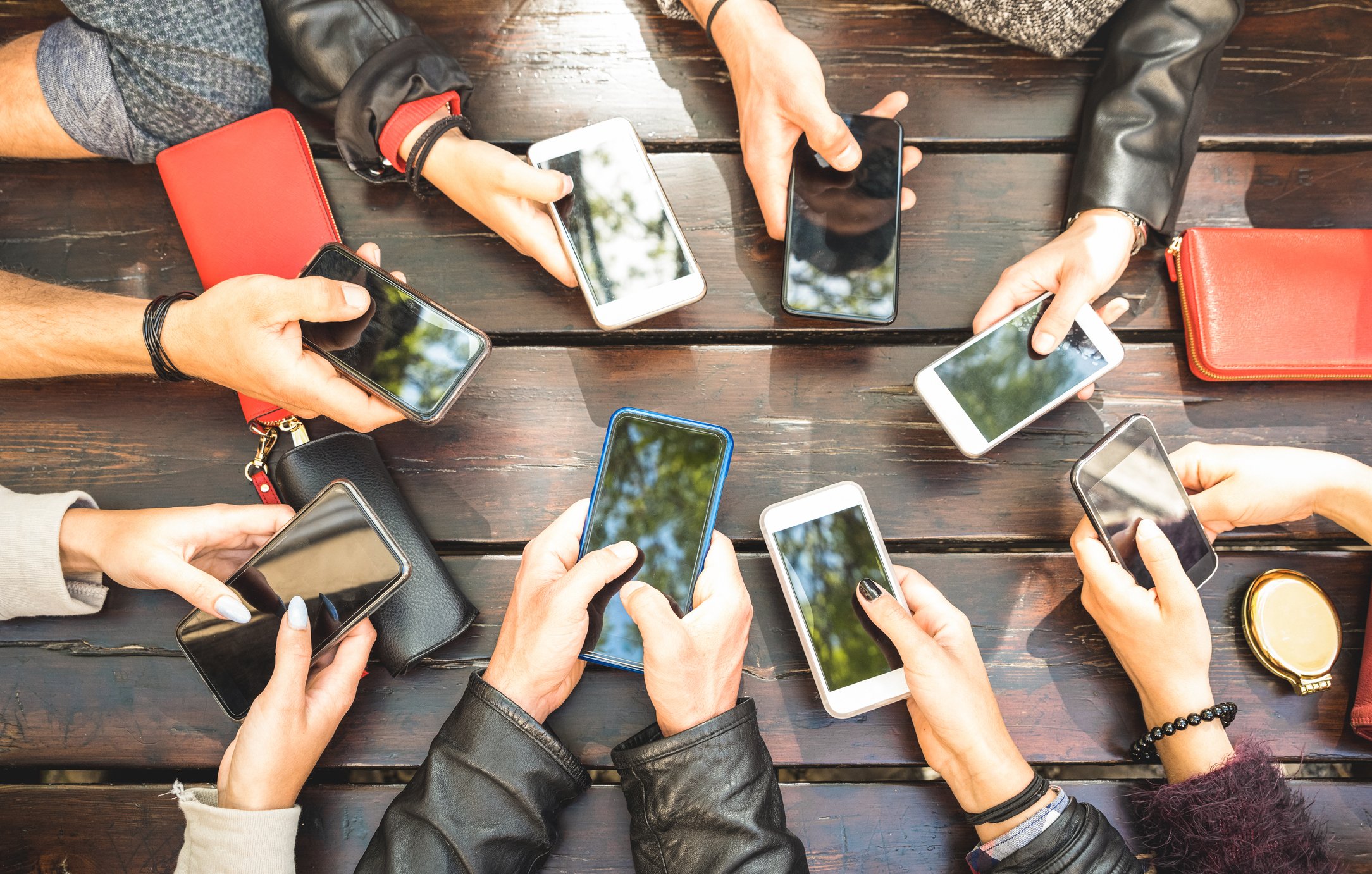 A group of hands holding mobile phones in a circle around a table.