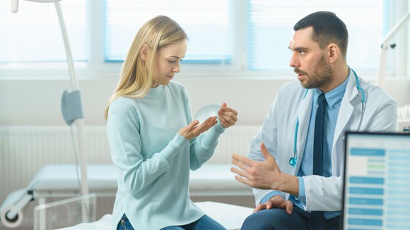 Patient and doctor looking at a breast implant in an exam room