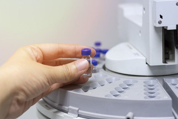 Hand holding small bottle next to chromatography equipment