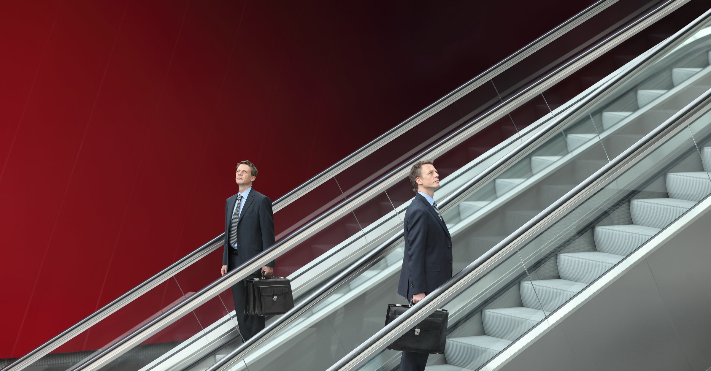 Businessmen going up and down two escalators