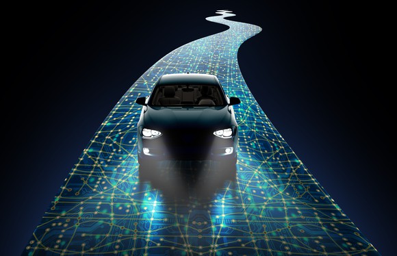 A self driving car seen from the  front drives through the dark on a sensored road with headlights on.