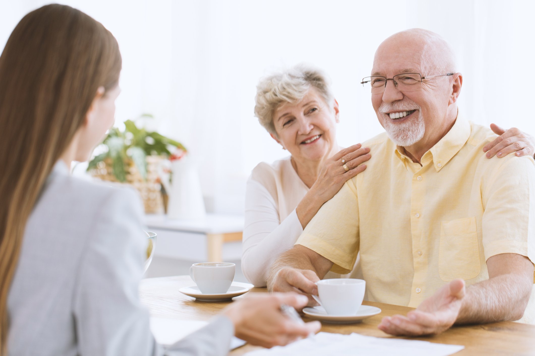 Young woman sitting across from smiling older couple with mugs in front of them