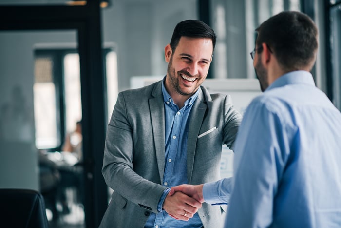 Two men shaking hands and smiling.