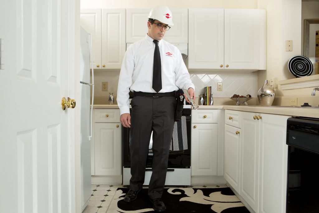 Orkin Man holding a flashlight and examining a kitchen.