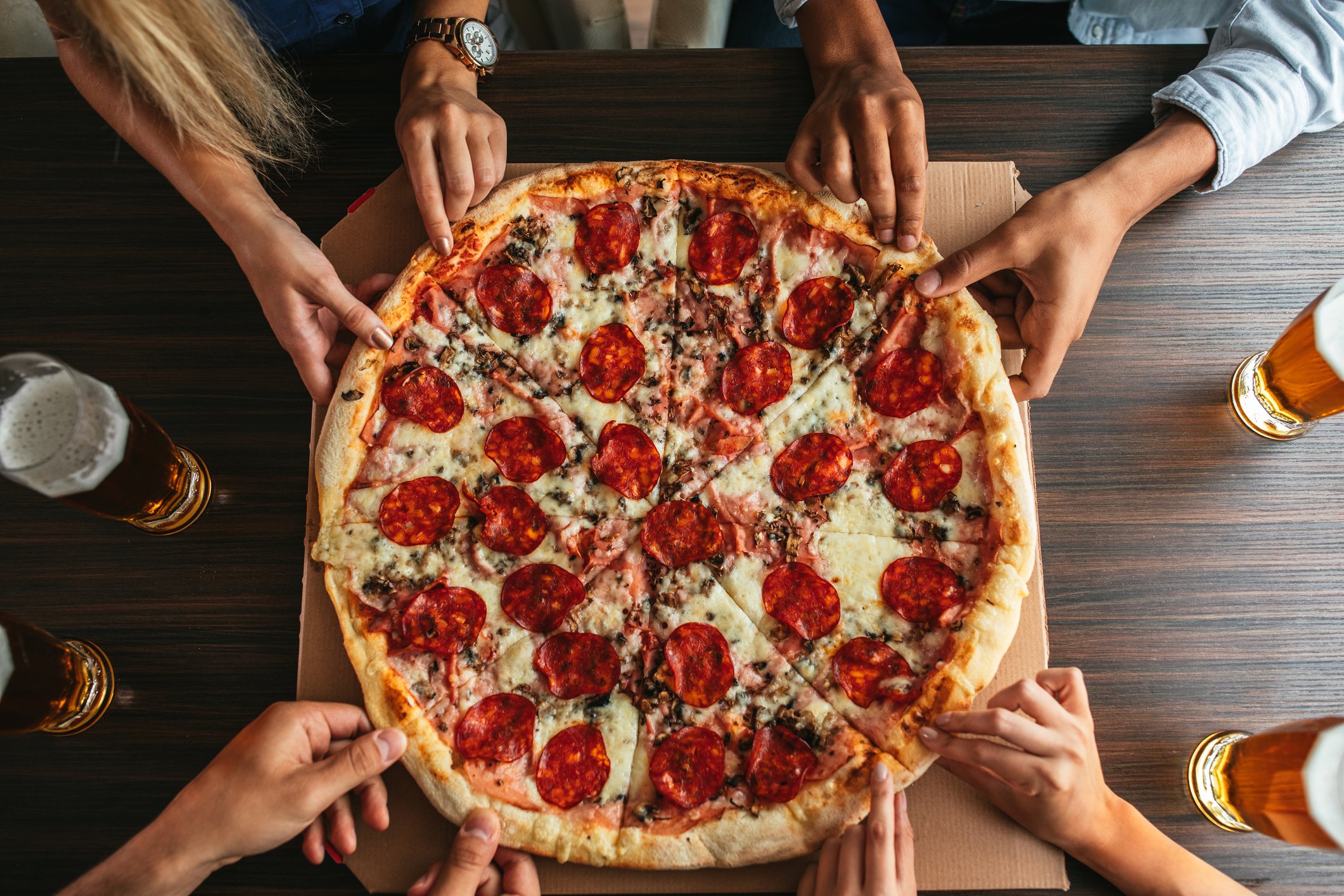 Hands grabbing for a large pizza pie.