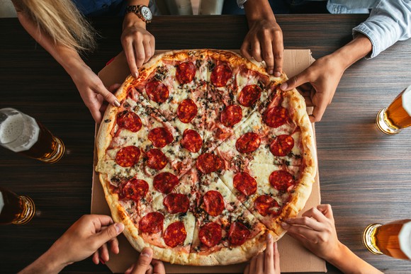 Hands grabbing for a large pizza pie.