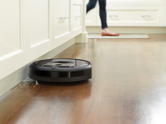 Roomba i7 sweeping crumbs from along a baseboard on a wood floor