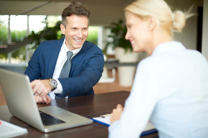 Two smiling business people share information on a laptop screen.