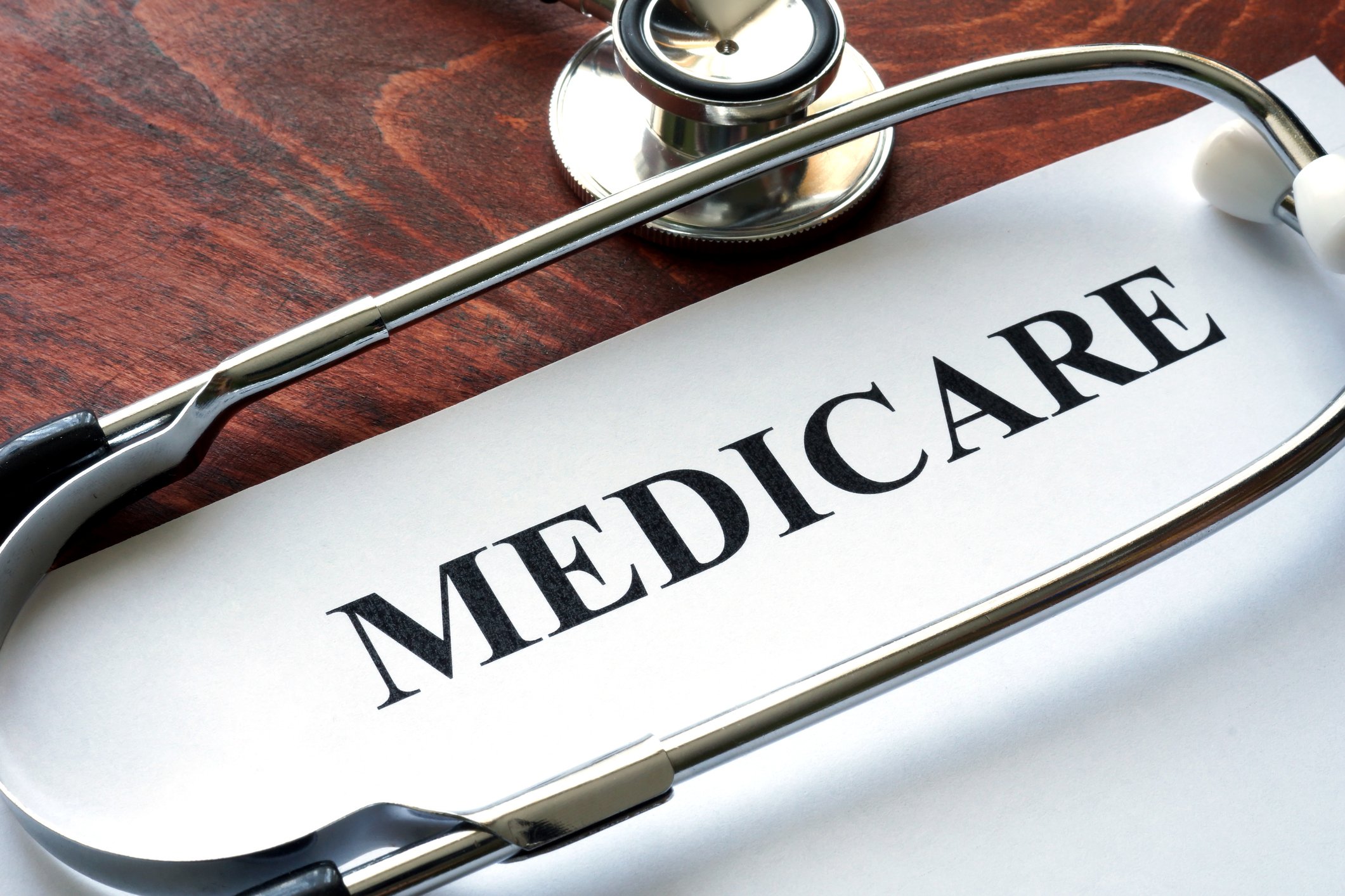 Paper titled "Medicare" with a stethoscope, both on a wood table.