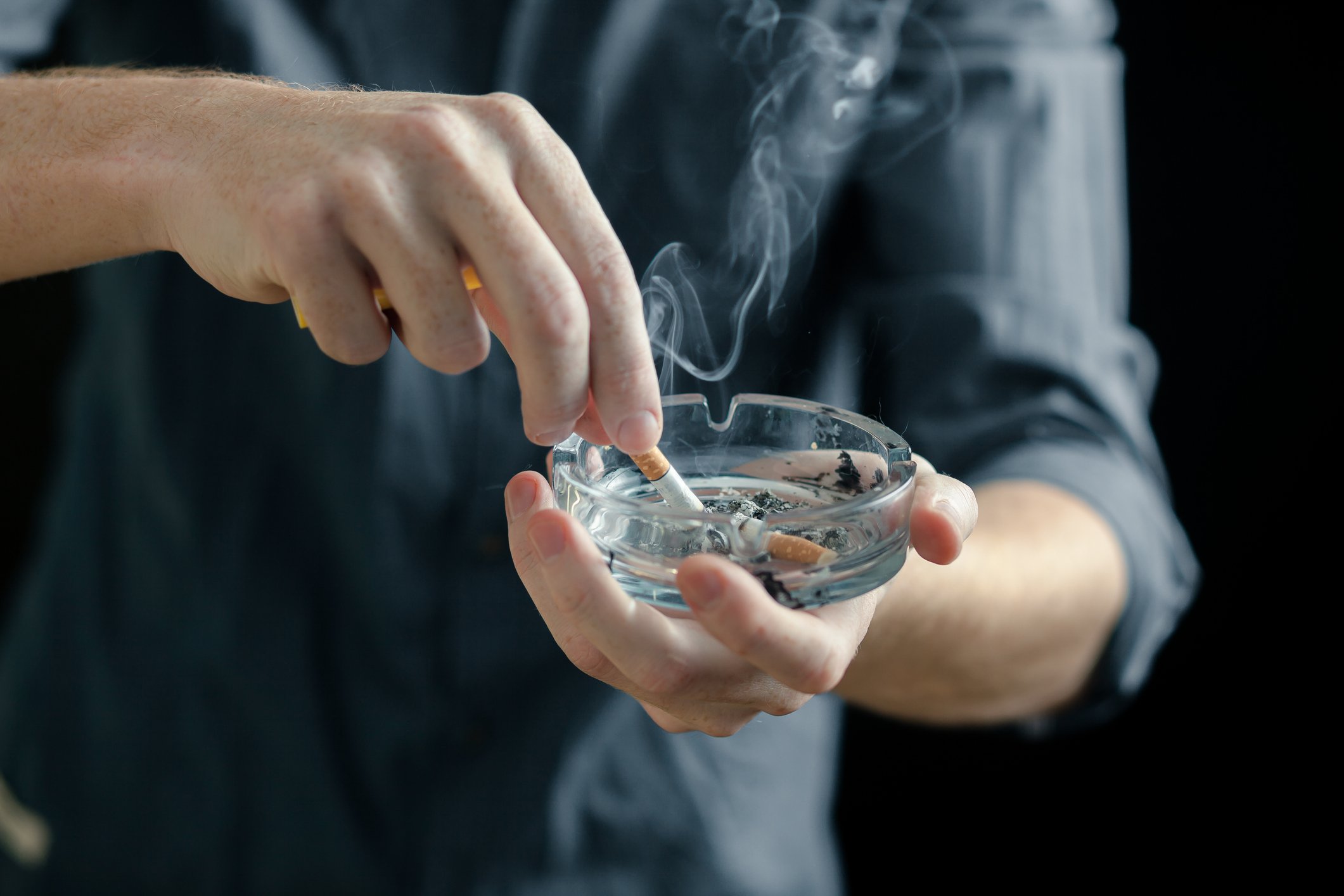 Man stubbing out a cigarette in an ashtray.