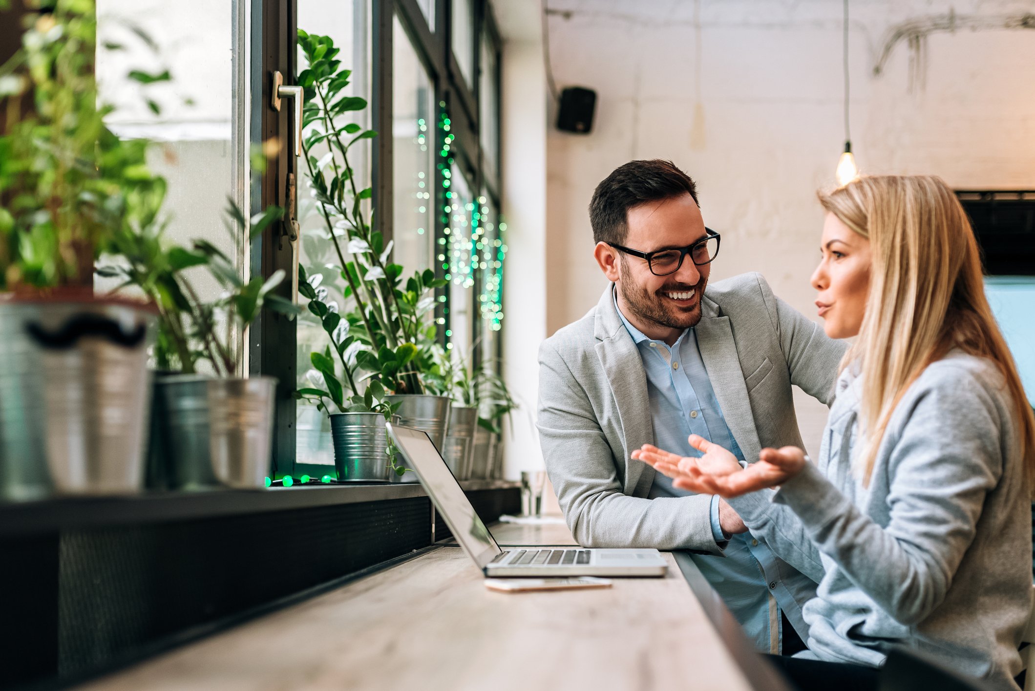 Professionally dressed man and woman talking, with laptop on table next to them