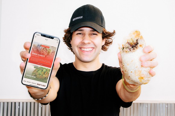 Person holding smartphone and Chipotle burrito.
