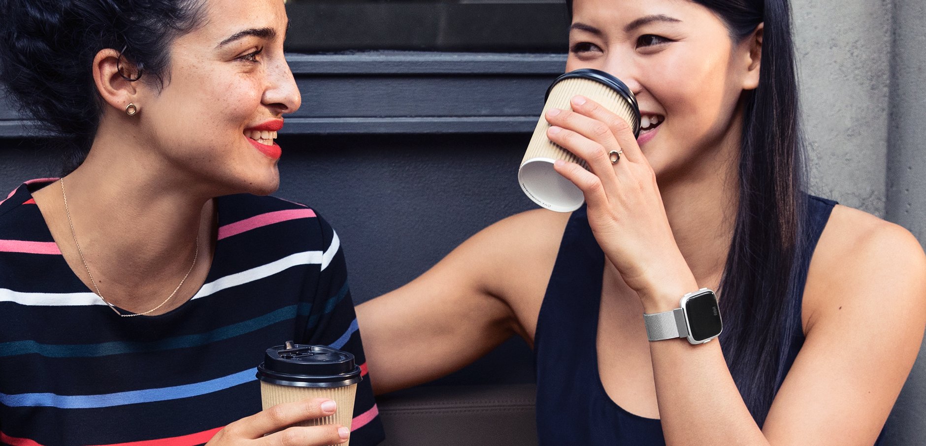 Women drinking coffee wearing Versa smartwatches