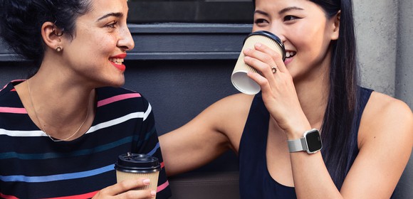 Women drinking coffee wearing Versa smartwatches