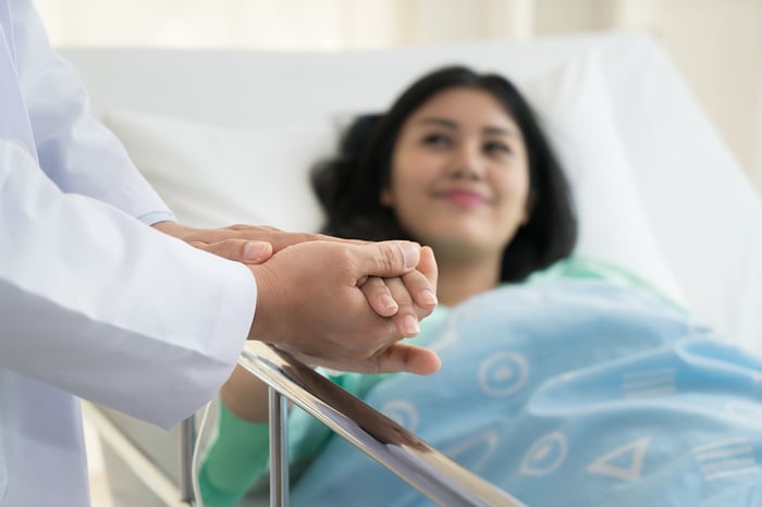 Patient in a hospital bed holding doctor's hand.