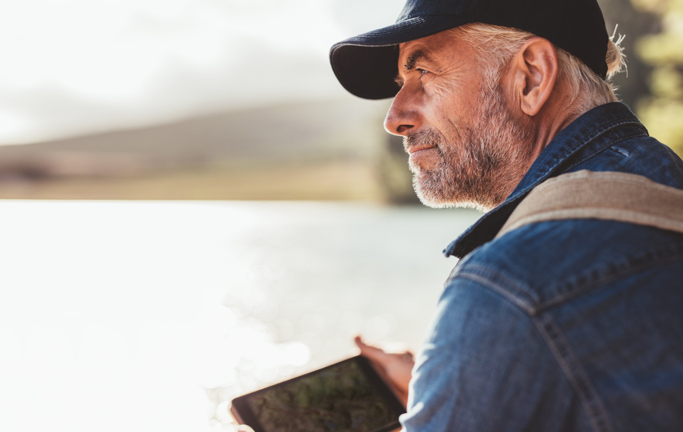 Older man in cap holding tablet outdoors