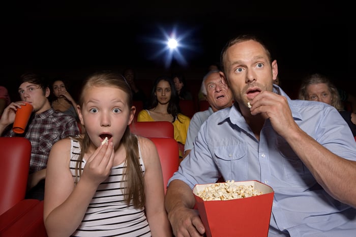 A father and his daughter eat popcorn while watching a movie.