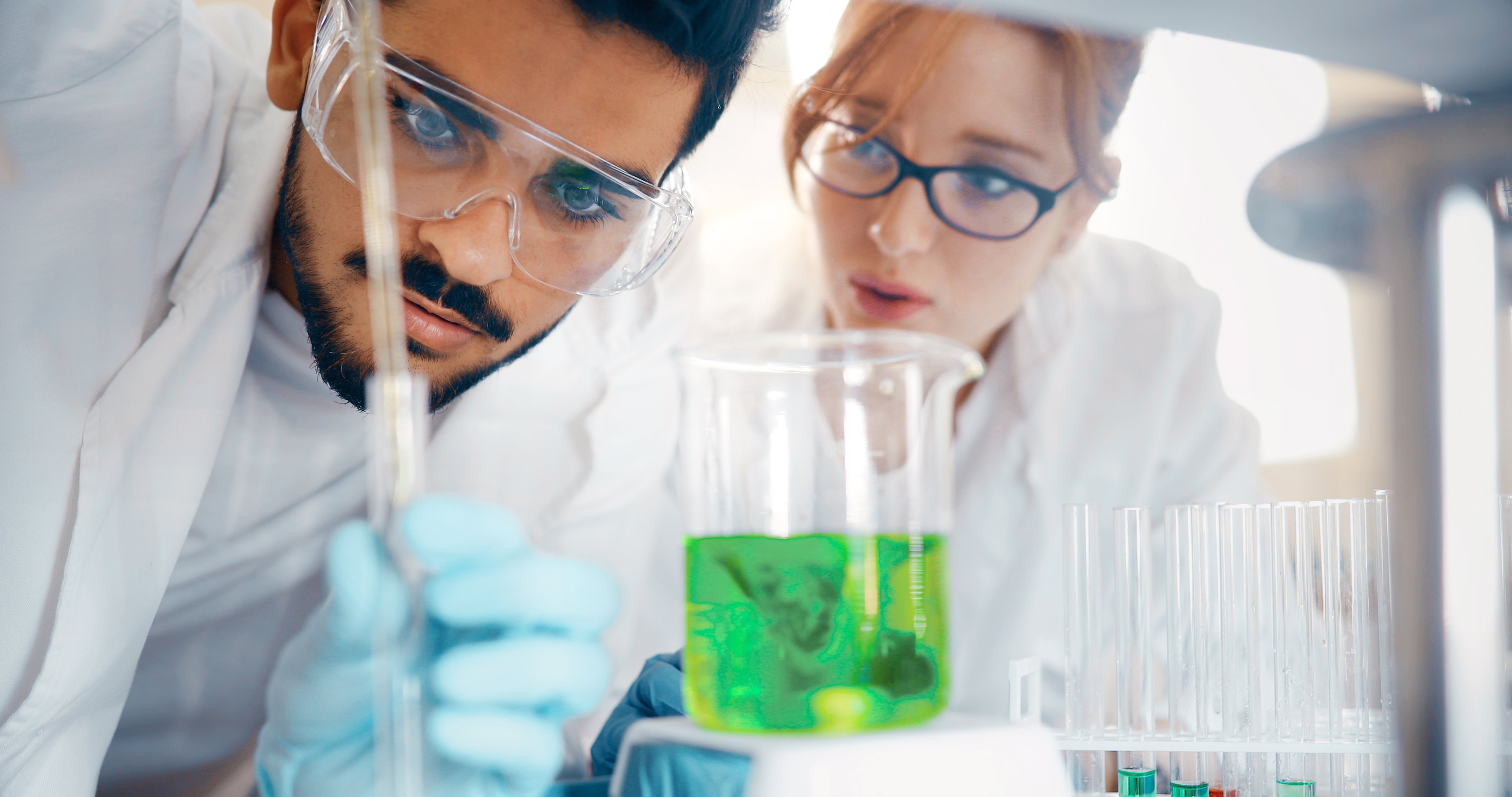 Scientists in lab looking at a beaker with green fluid