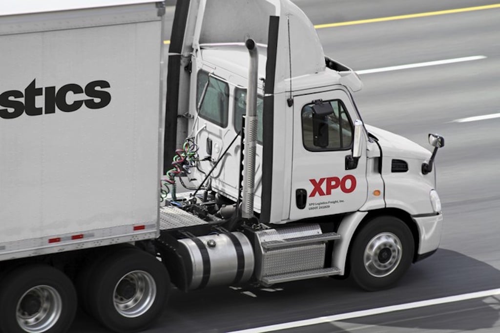 White truck with XPO branding on the side in the right lane of a four-lane highway.