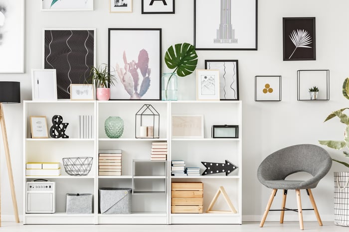 Grey armchair next to a white shelving unit with books and decorations. Art hangs on the wall behind them.