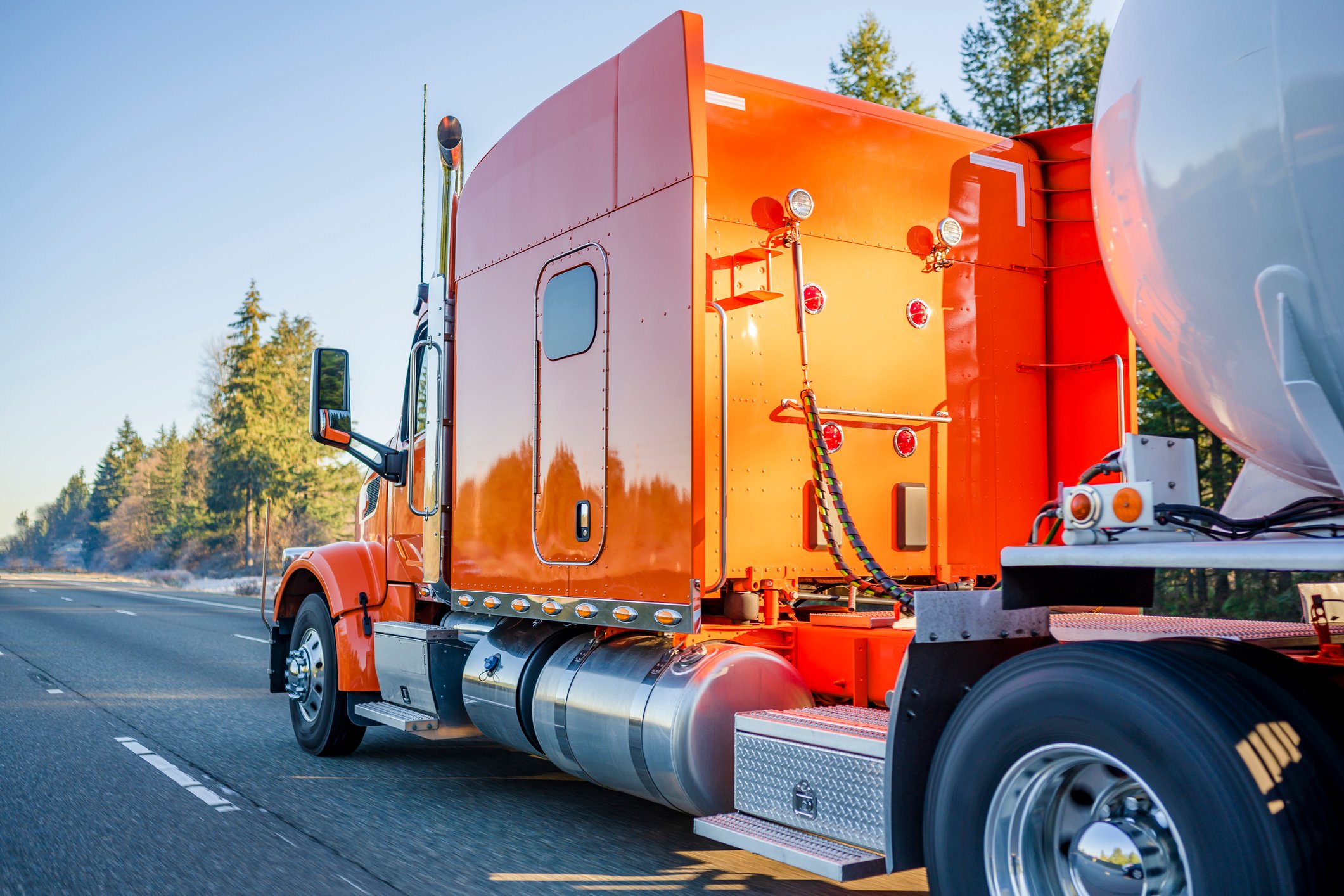Big orange semi truck hauling a tanker of liquified gas.