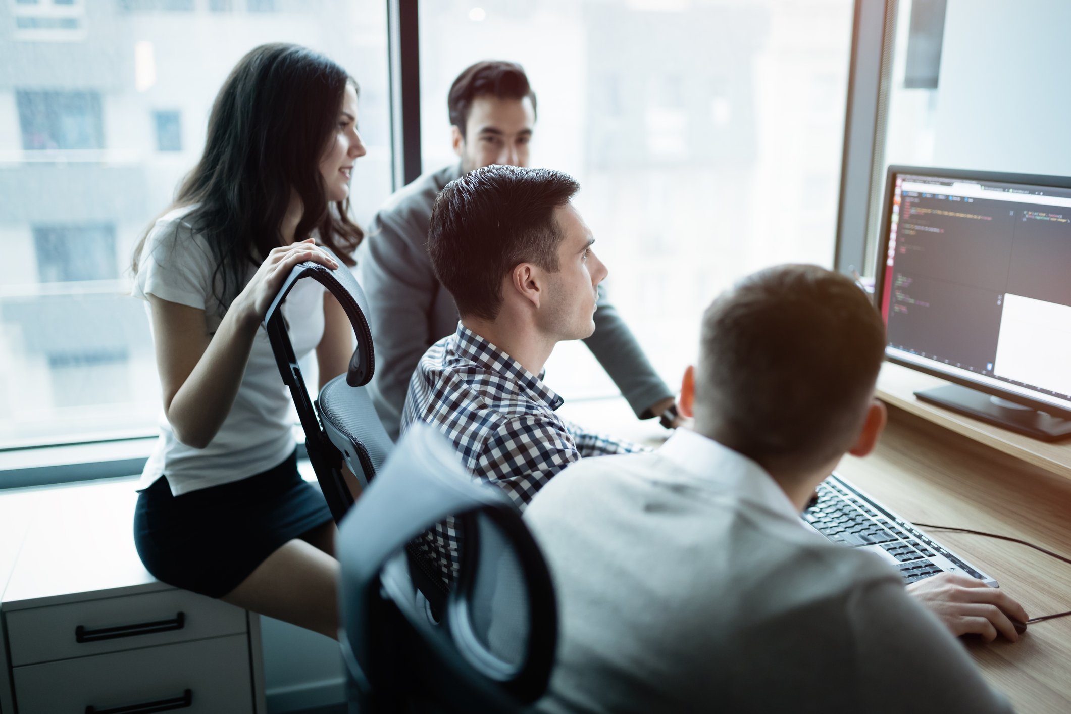Business people sitting around a computer with code on the screen.