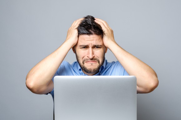 Man at laptop with sad expression holding his head with both hands