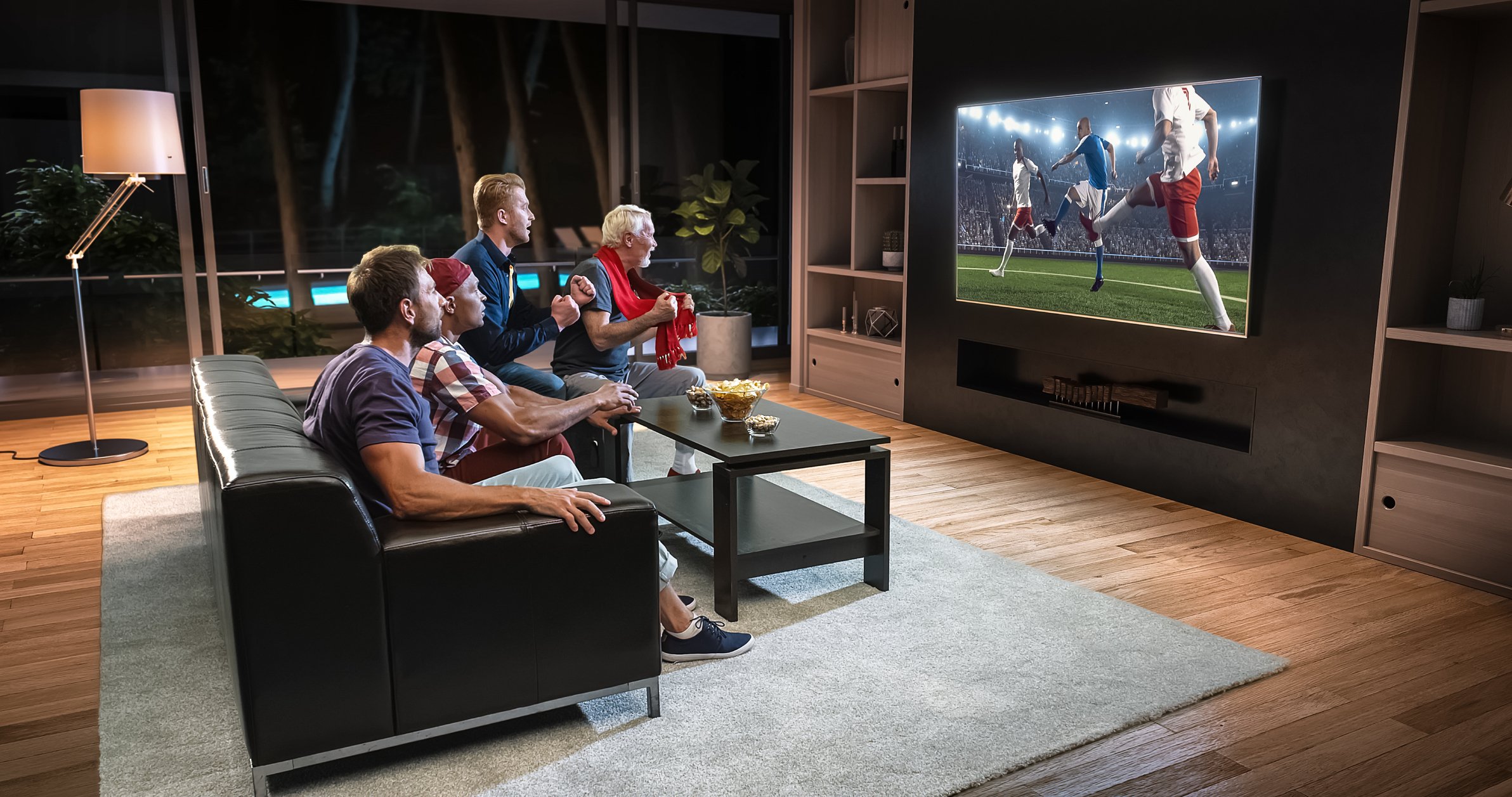 A family sits in a living room watching soccer on a big screen TV.